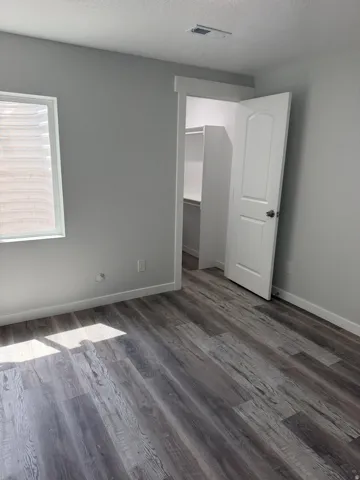 Spacious room featuring wood-finish flooring, a bright window, and a built-in closet with shelving