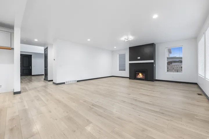 Spacious room featuring light wood-finish flooring, a modern black fireplace surround with a white mantel, recessed lighting, and multiple windows
