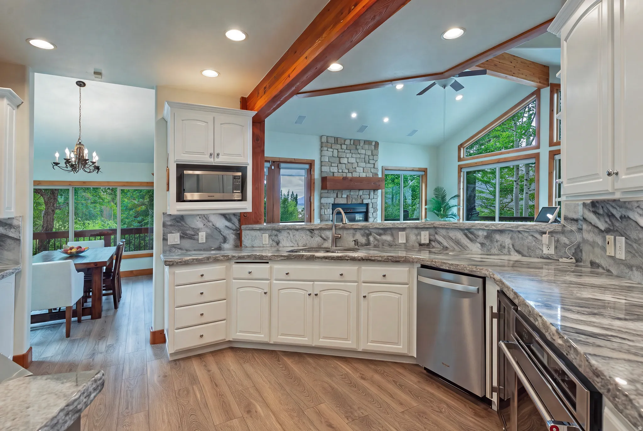Kitchen featuring light wood-finish flooring, white cabinetry, integrated stainless steel appliances, and gray veined countertops with matching backsplash