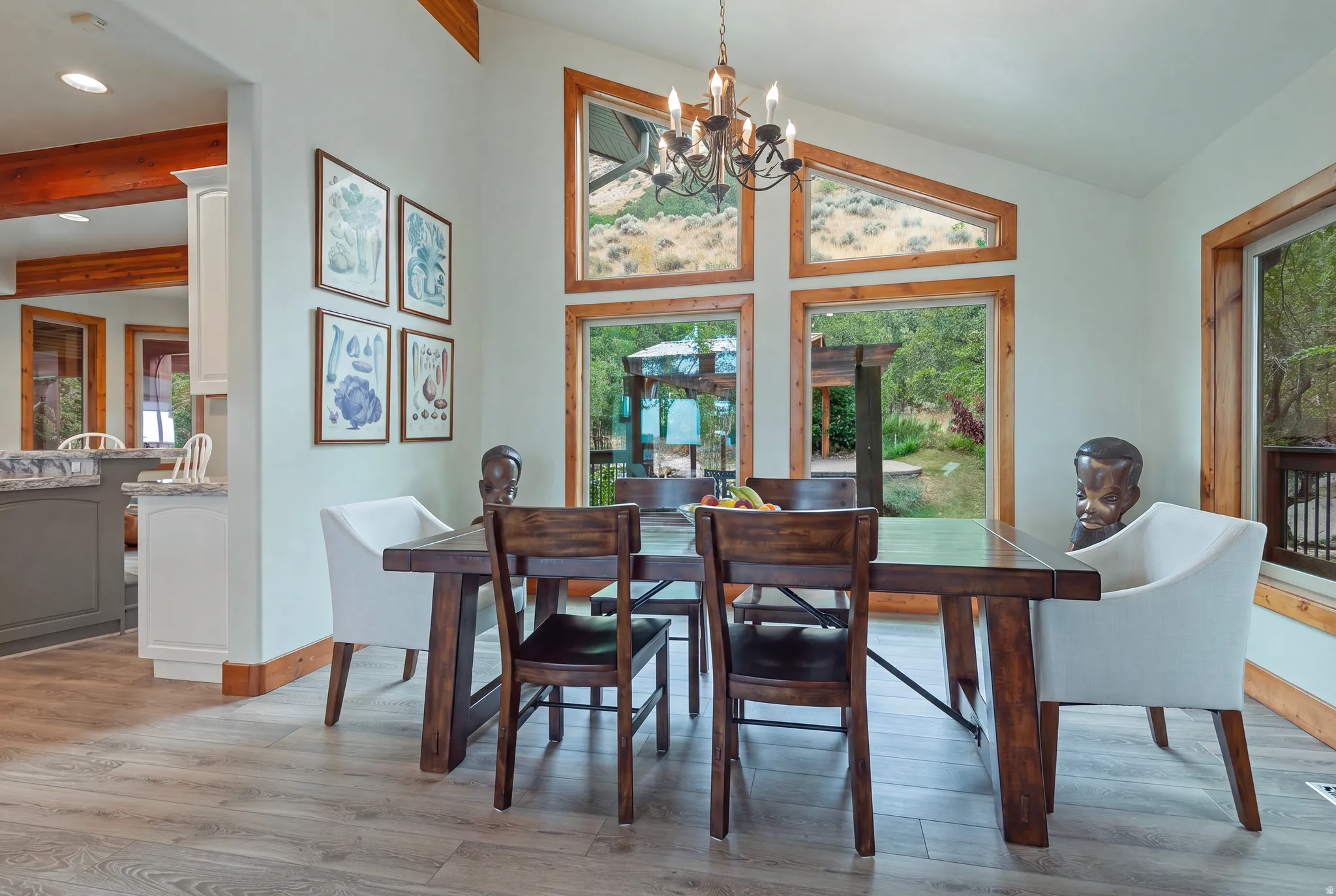 Dining area with vaulted ceilings, featuring large picture windows, wood-finish trim, and light wood-finish flooring