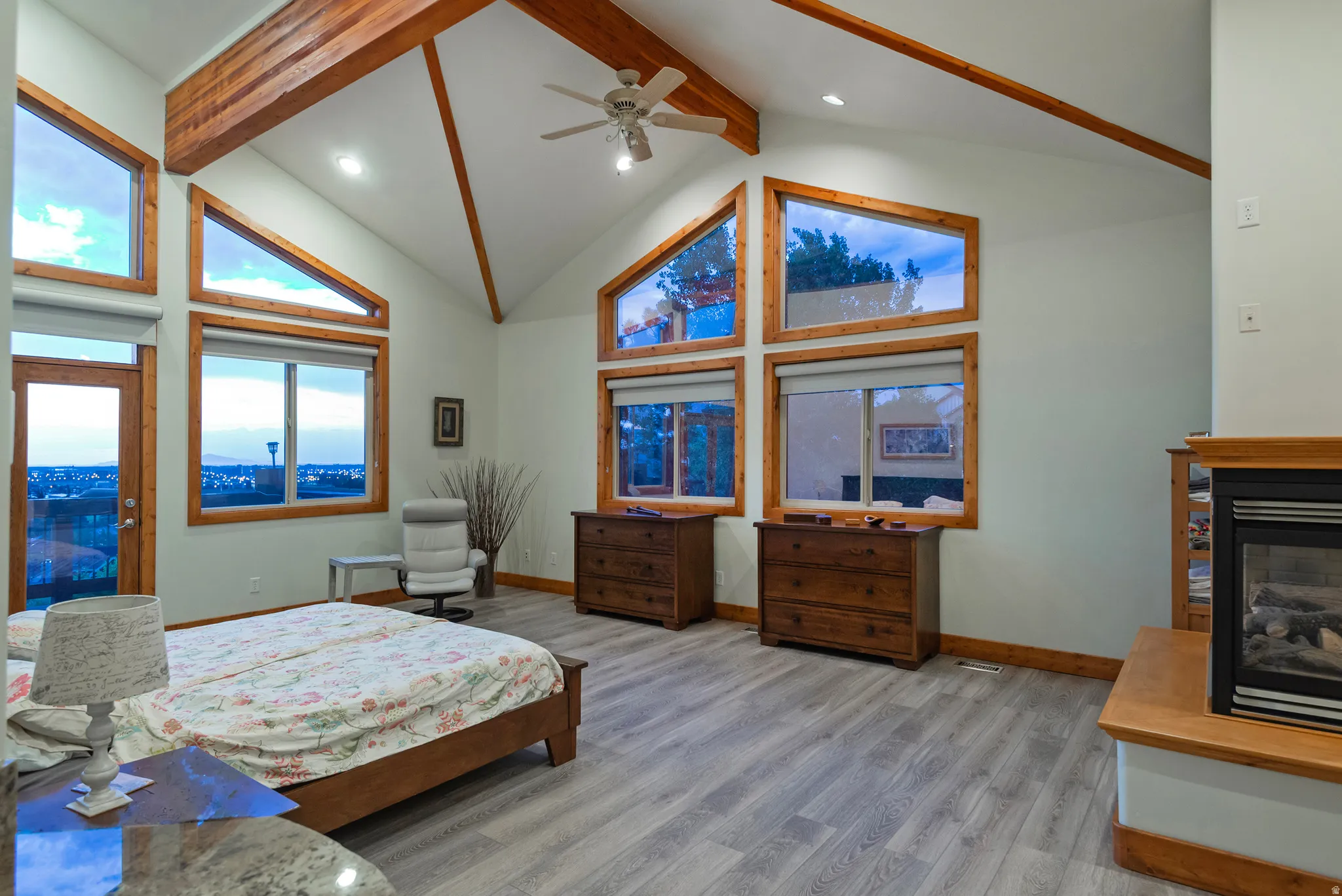 Vaulted ceiling with exposed wood beams, LVP flooring, multiple large windows, and a built-in fireplace with wood mantle