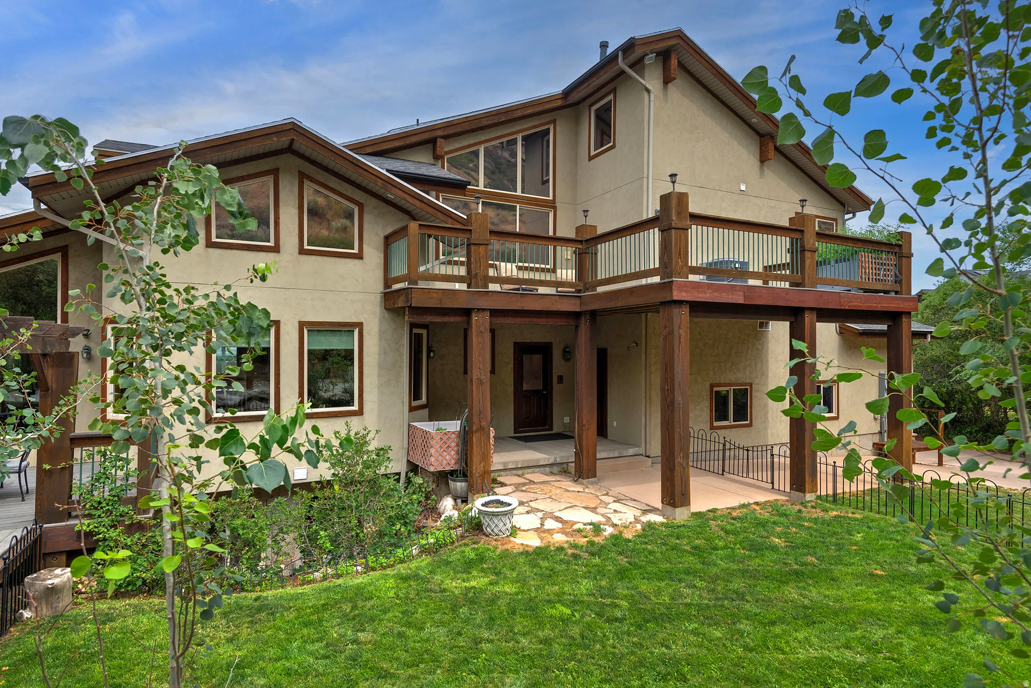 Multi-level exterior featuring stucco siding, expansive wood decks with railings, a stone patio, and a sloped lawn area