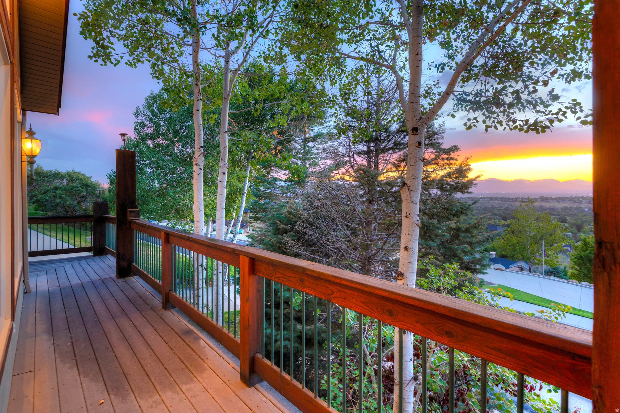 Spacious outdoor deck featuring wood-finish flooring, a sturdy wood railing with metal balusters, and an attached exterior wall lantern
