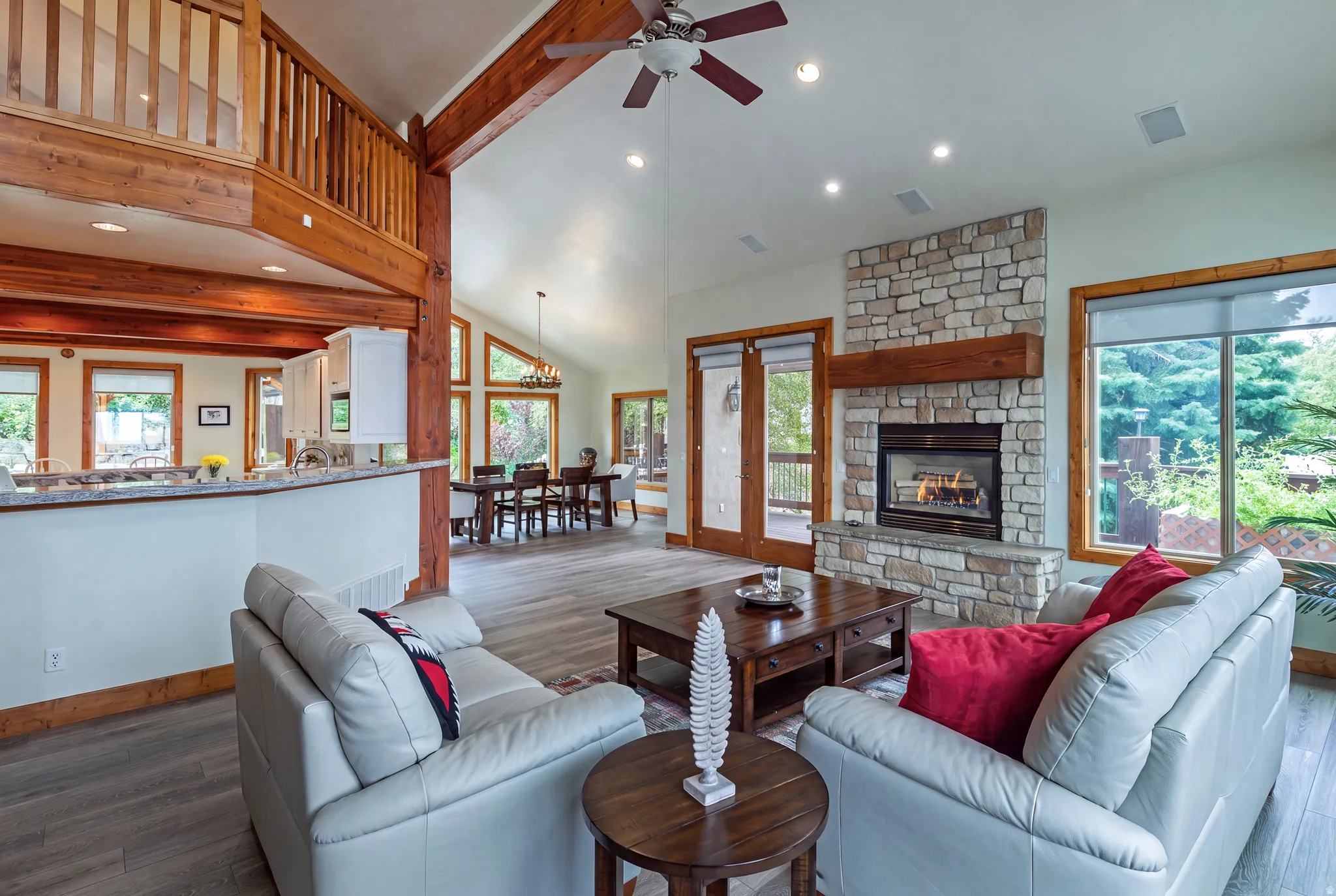 Vaulted ceiling living area featuring a stone fireplace with wood mantel, wood-finish flooring, exposed wood beams, and a second-story open balcony