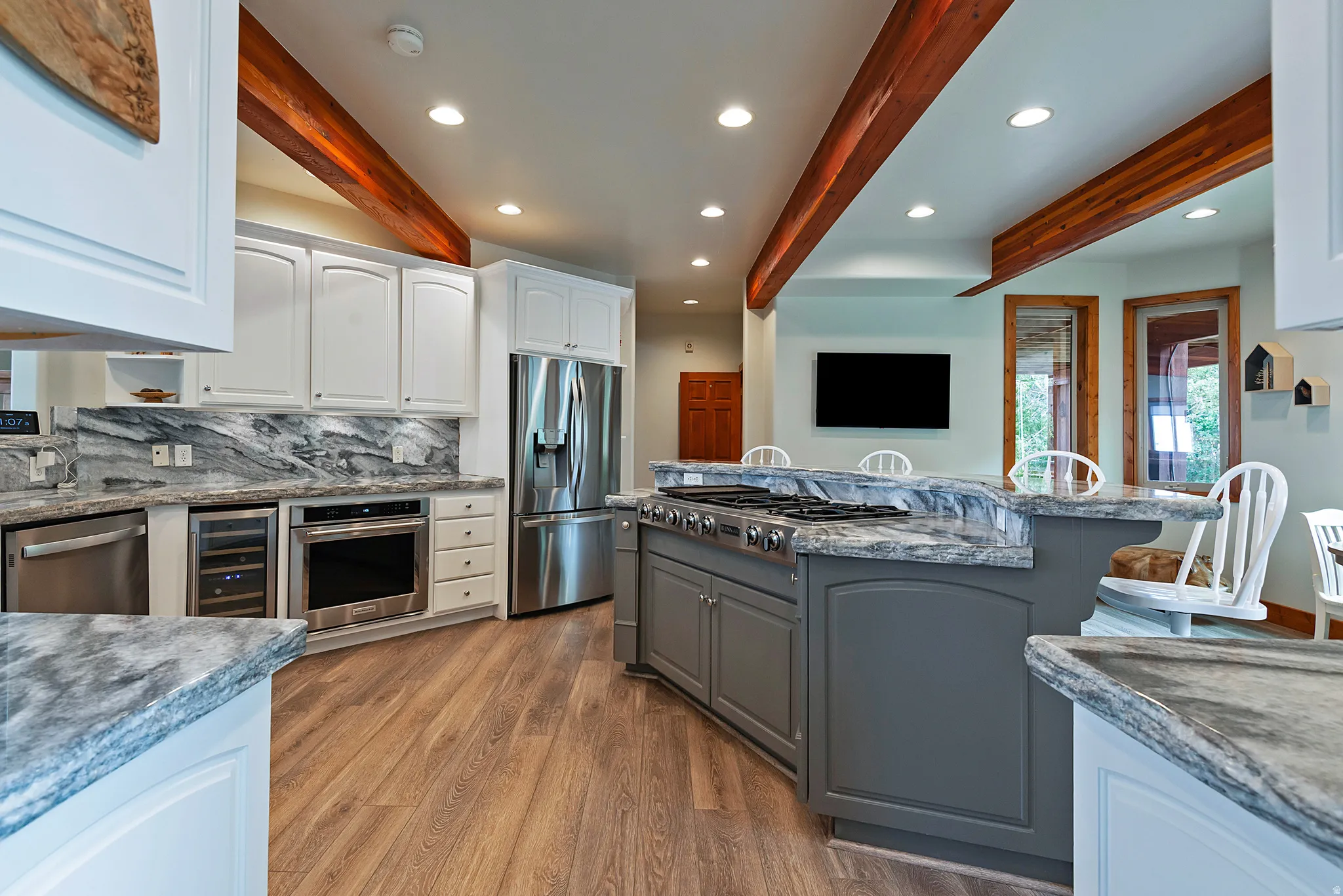 Vaulted ceiling kitchen featuring exposed wood beams, wood-finish flooring, stainless steel appliances, a center island with a built-in range, and a breakfast bar