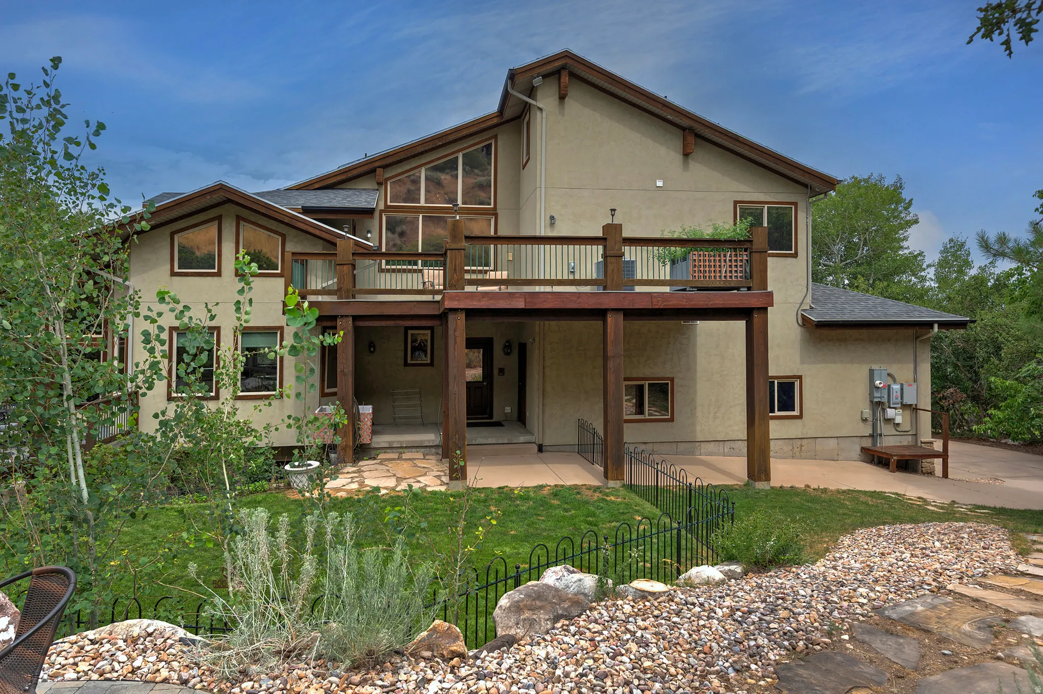 Multi-level stucco residence featuring a ground-level patio and an elevated deck with wood railings