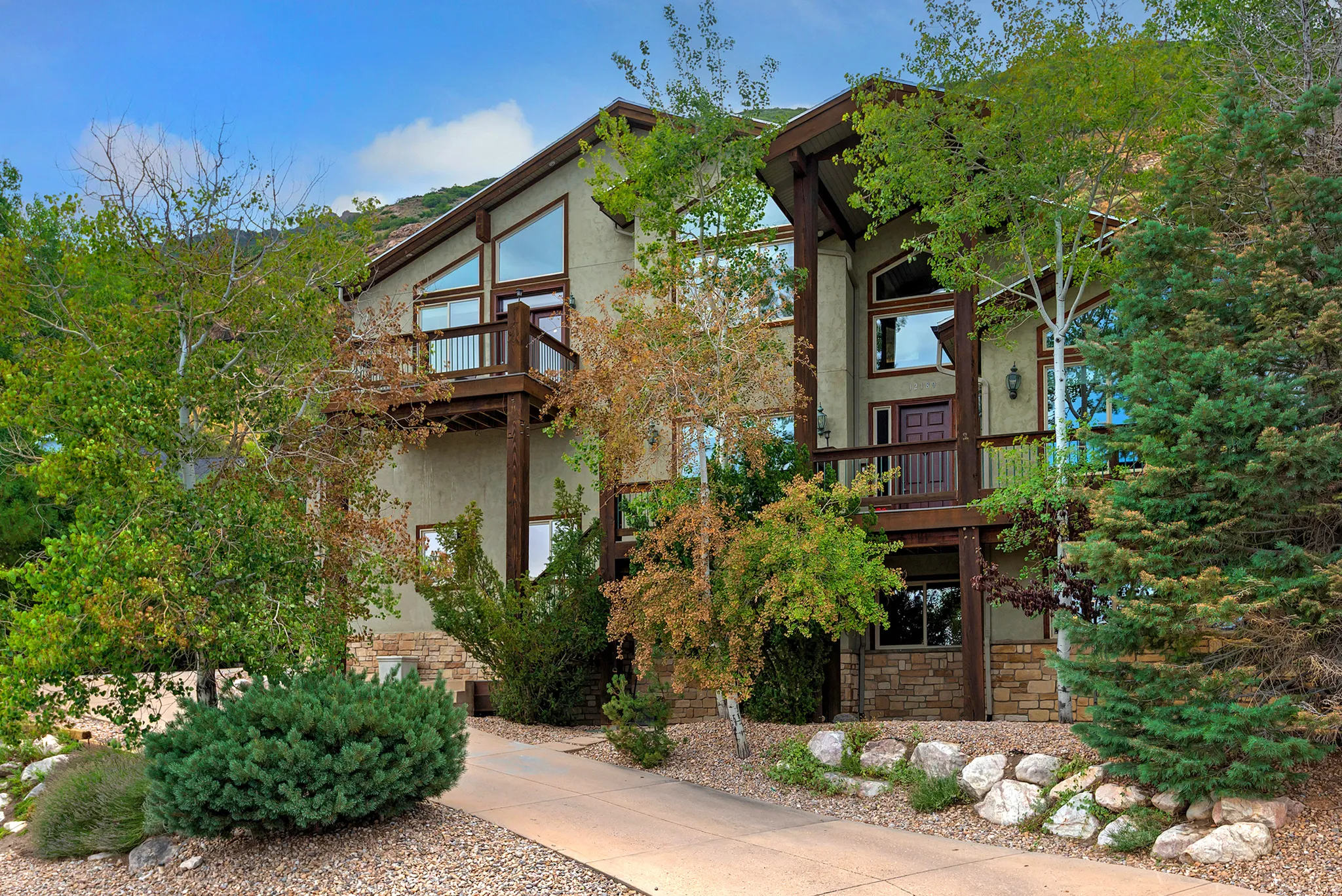 Multi-level residence featuring expansive window walls, stucco and stone veneer siding, and a prominent front entry with an upper-level balcony