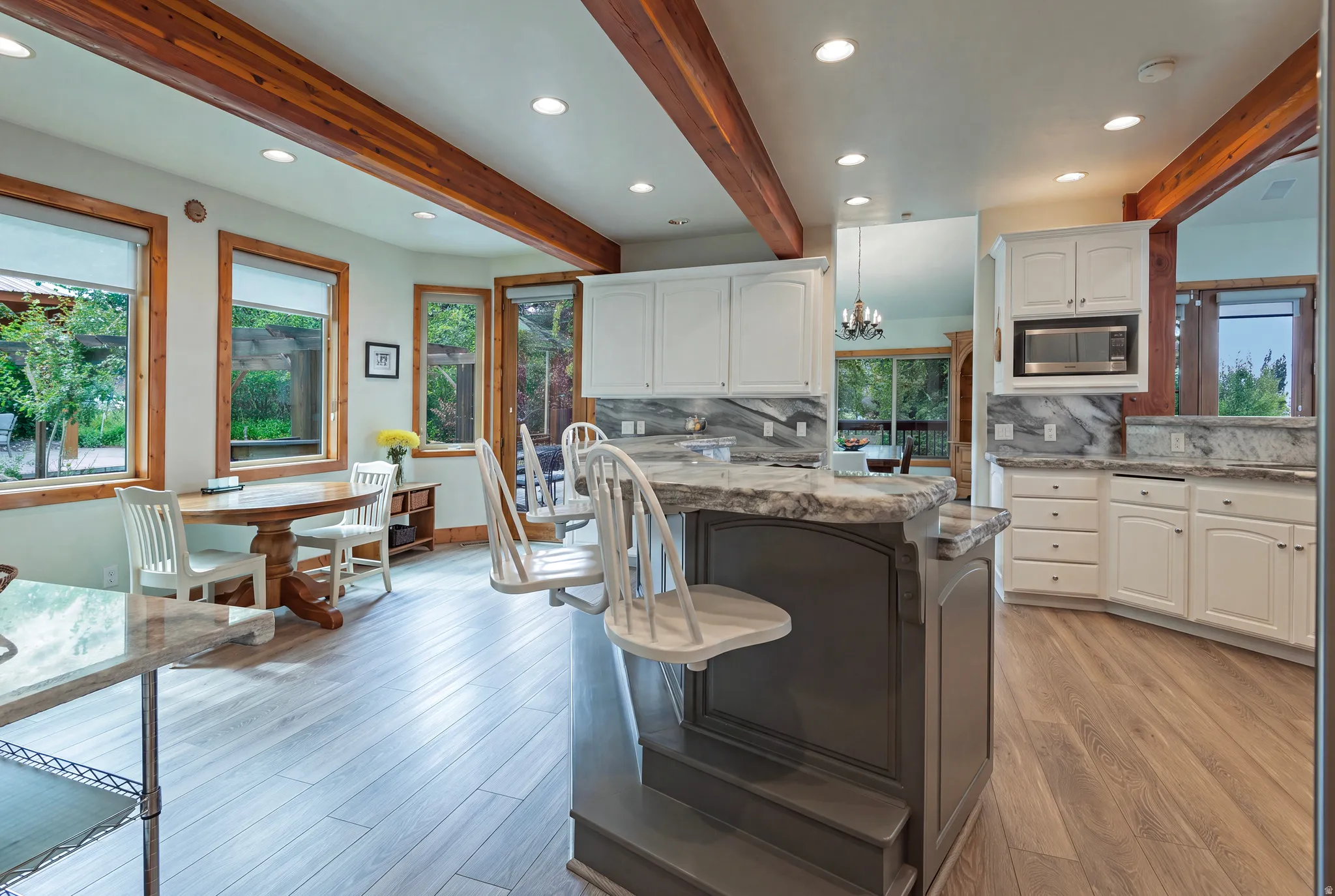Spacious kitchen featuring an island with seating, extensive white cabinetry, light wood-finish flooring, recessed lighting, and exposed wood beams
