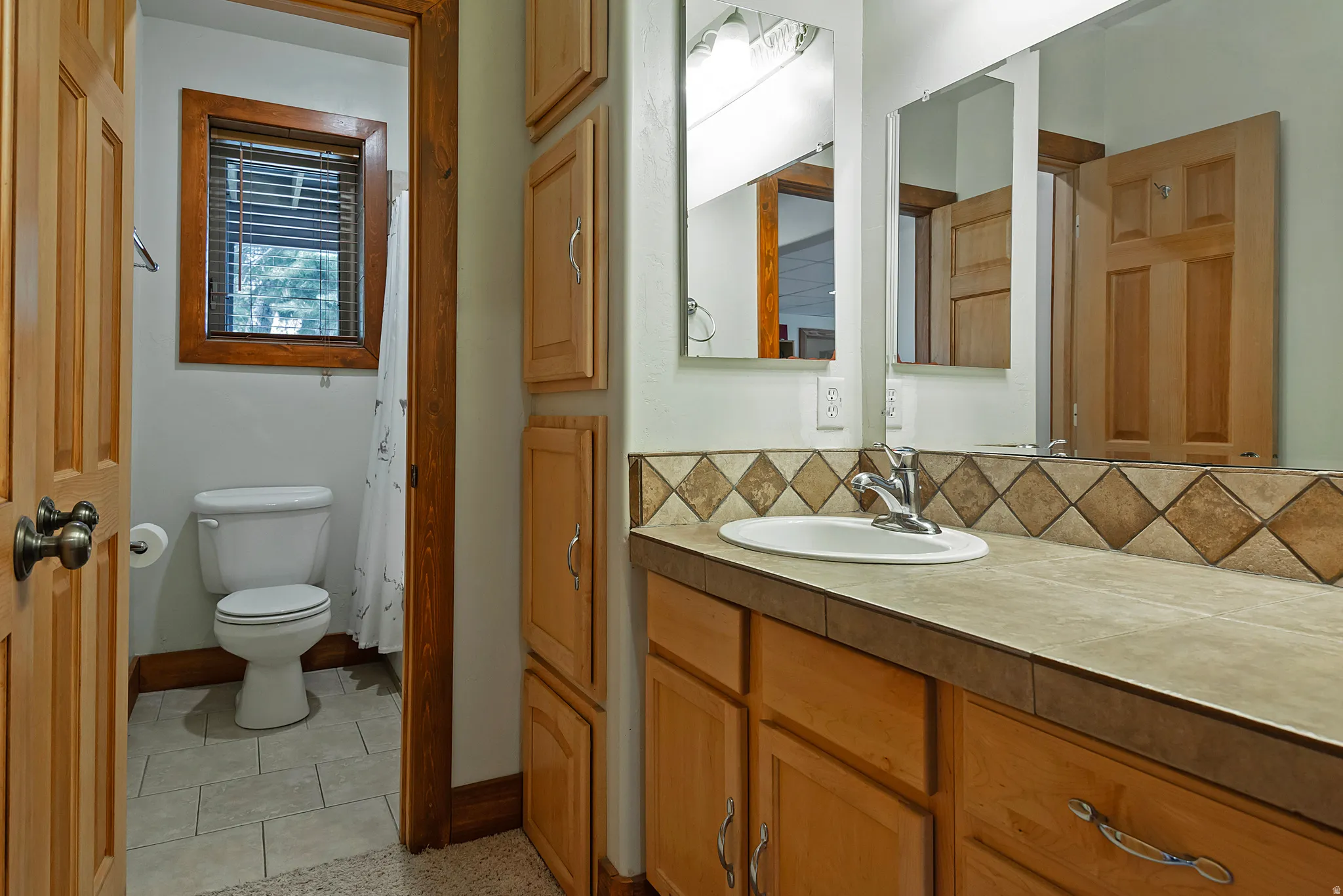 Bathroom vanity featuring an oval undermount sink, chrome faucet, and tiled countertop with a decorative backsplash