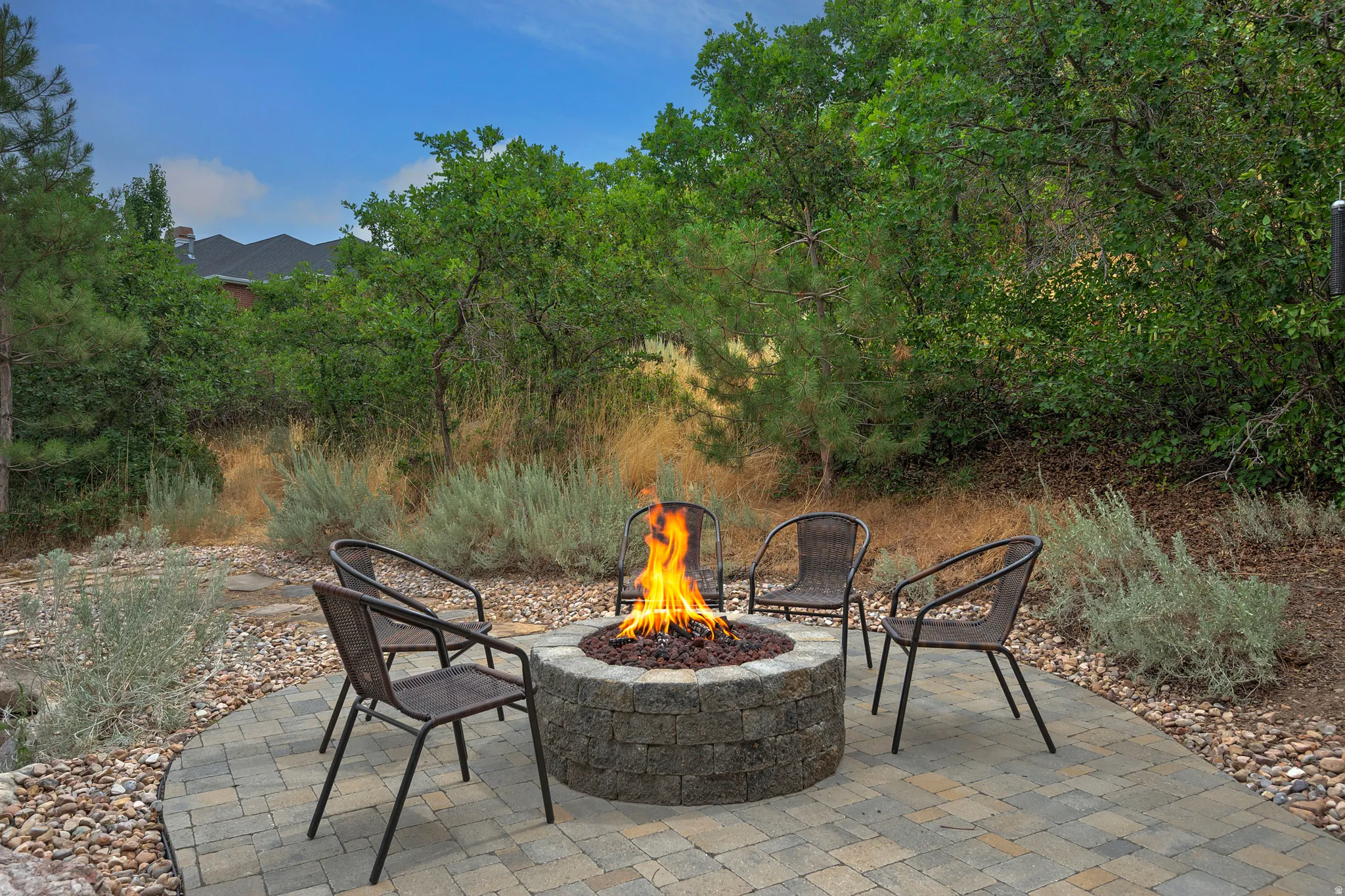Paver patio with a built-in stone fire pit, surrounded by natural landscaping and mature trees