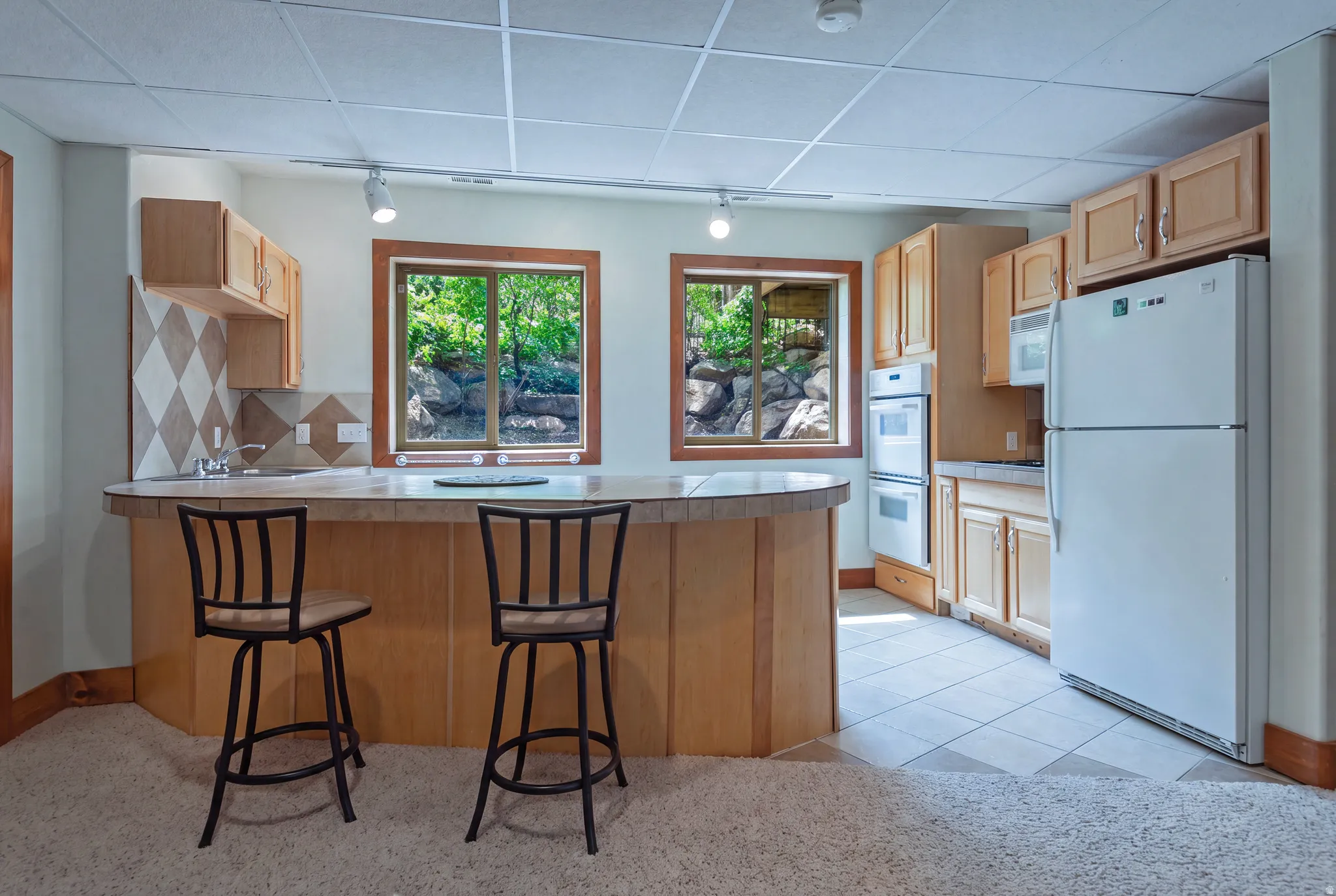 Kitchenette featuring wood cabinetry, built-in double ovens, and a tile backsplash with a diamond pattern