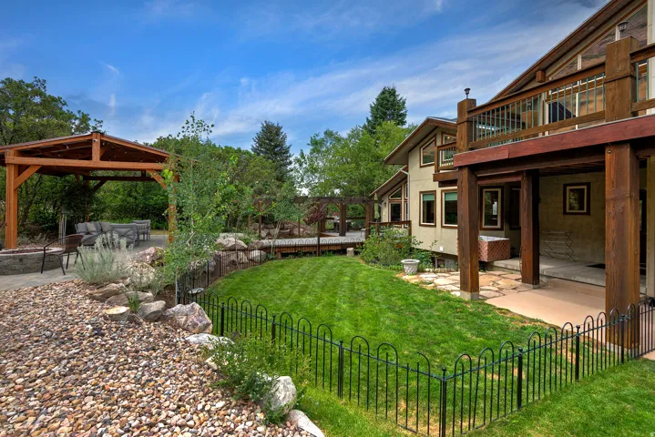 Expansive outdoor living area featuring a covered patio with a built-in fire pit, a lower-level grass area, an upper-level wood deck, a second-story balcony, and a multi-level rock garden