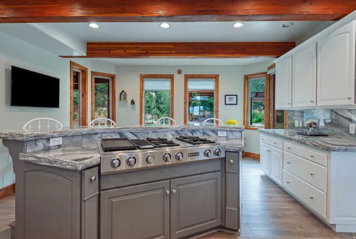 Kitchen featuring a built-in range on a grey-painted island, white cabinetry, integrated stainless steel appliances, wood-finish flooring, and exposed ceiling beams
