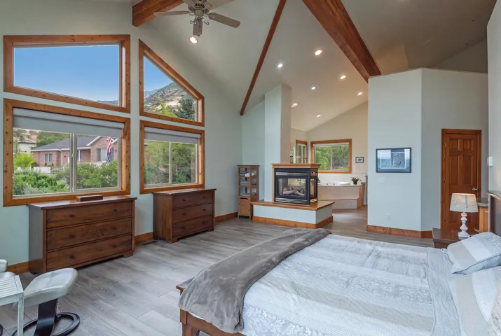 Vaulted ceiling with exposed wood beams, a central fireplace, and wood-finish flooring