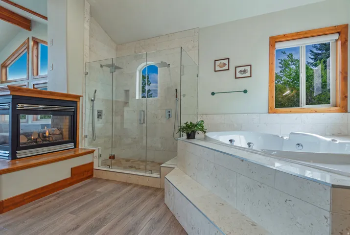 Freestanding soaking tub with tiled surround, adjacent to a glass-enclosed shower featuring a tiled interior and built-in niche