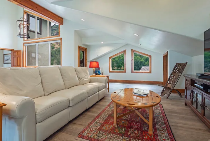 Spacious living area featuring light wood-finish flooring, a vaulted ceiling, exposed wood beams, and a large multi-pane window system