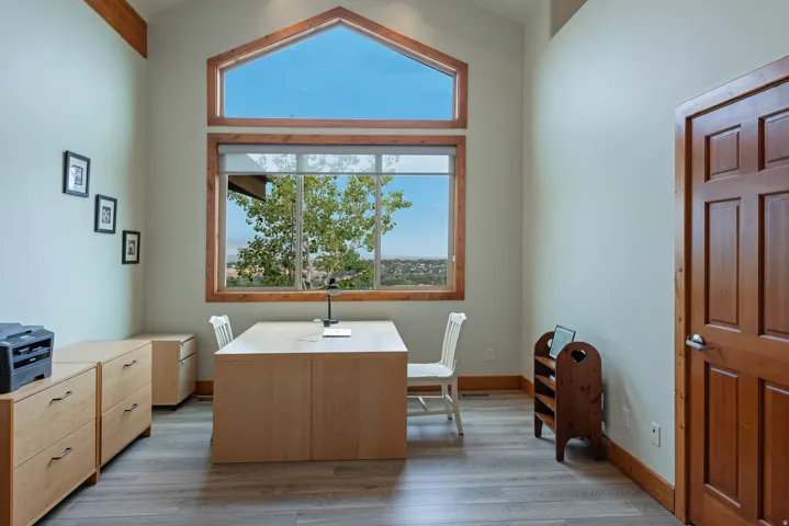 Vaulted ceiling room featuring a large picture window with an arched transom, wood-finish flooring, light-toned built-in cabinetry, and a solid wood paneled door