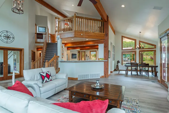 Vaulted ceilings featuring exposed wood beams, a prominent staircase with wood railings, and a second-story interior balcony