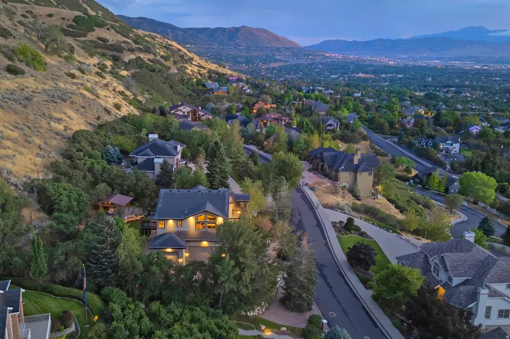 Hillside residence featuring a dark shingle roof, multiple gables, and illuminated windows