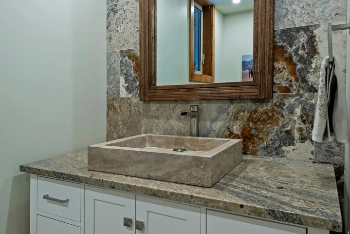 Modern vanity featuring a rectangular vessel sink, granite countertop, and a natural stone tile backsplash