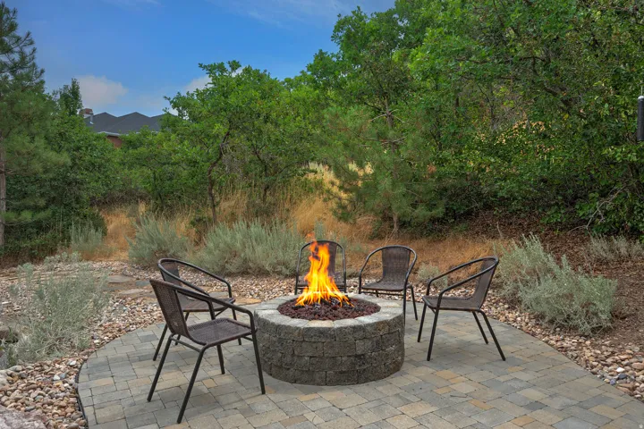 Paver patio with a built-in stone fire pit, surrounded by natural landscaping and mature trees