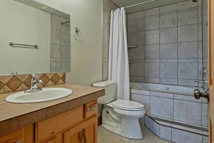 Bathroom featuring a wood-finish vanity with a tile countertop, an oval-shaped sink with a chrome faucet, and a wall-mounted mirror