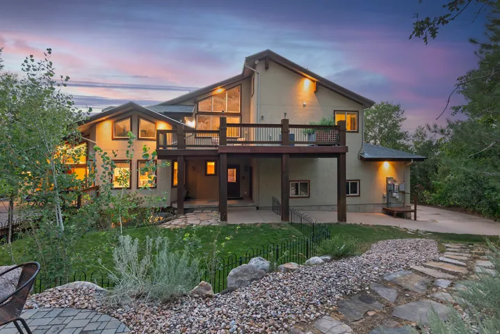 Multi-level residence featuring a prominent elevated deck with dark wood railing, extensive windows, and a stone-paved patio below