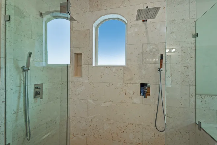 Tiled shower with glass enclosure featuring two arched windows, a built-in shower niche, a square rain showerhead, and a hand-held shower sprayer