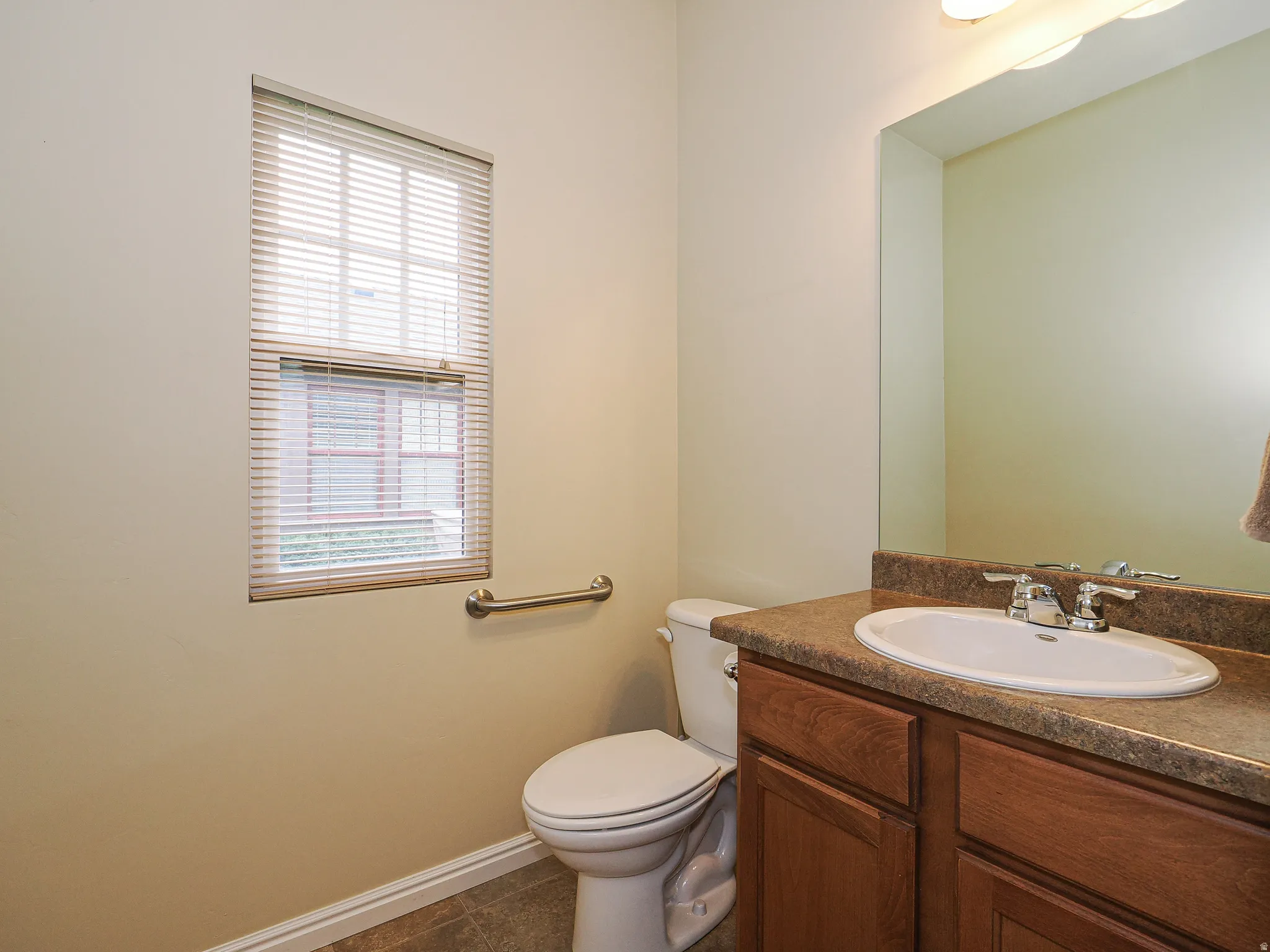 Bathroom featuring a vanity with a brown countertop and integrated sink, wood-finish cabinetry, a toilet, and a window with blinds