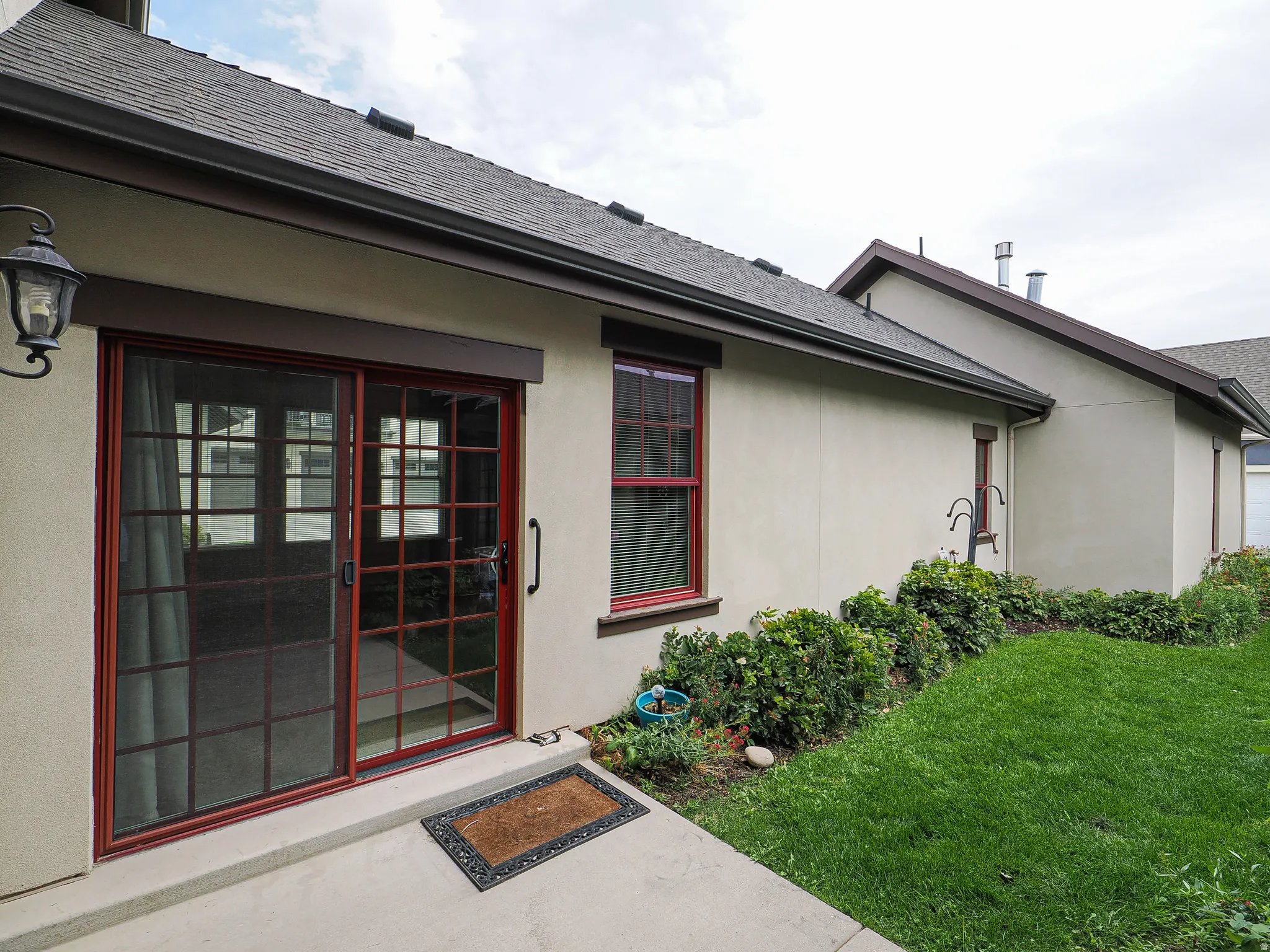 Patio with sliding glass door access, exterior wall sconce, and red-trimmed windows