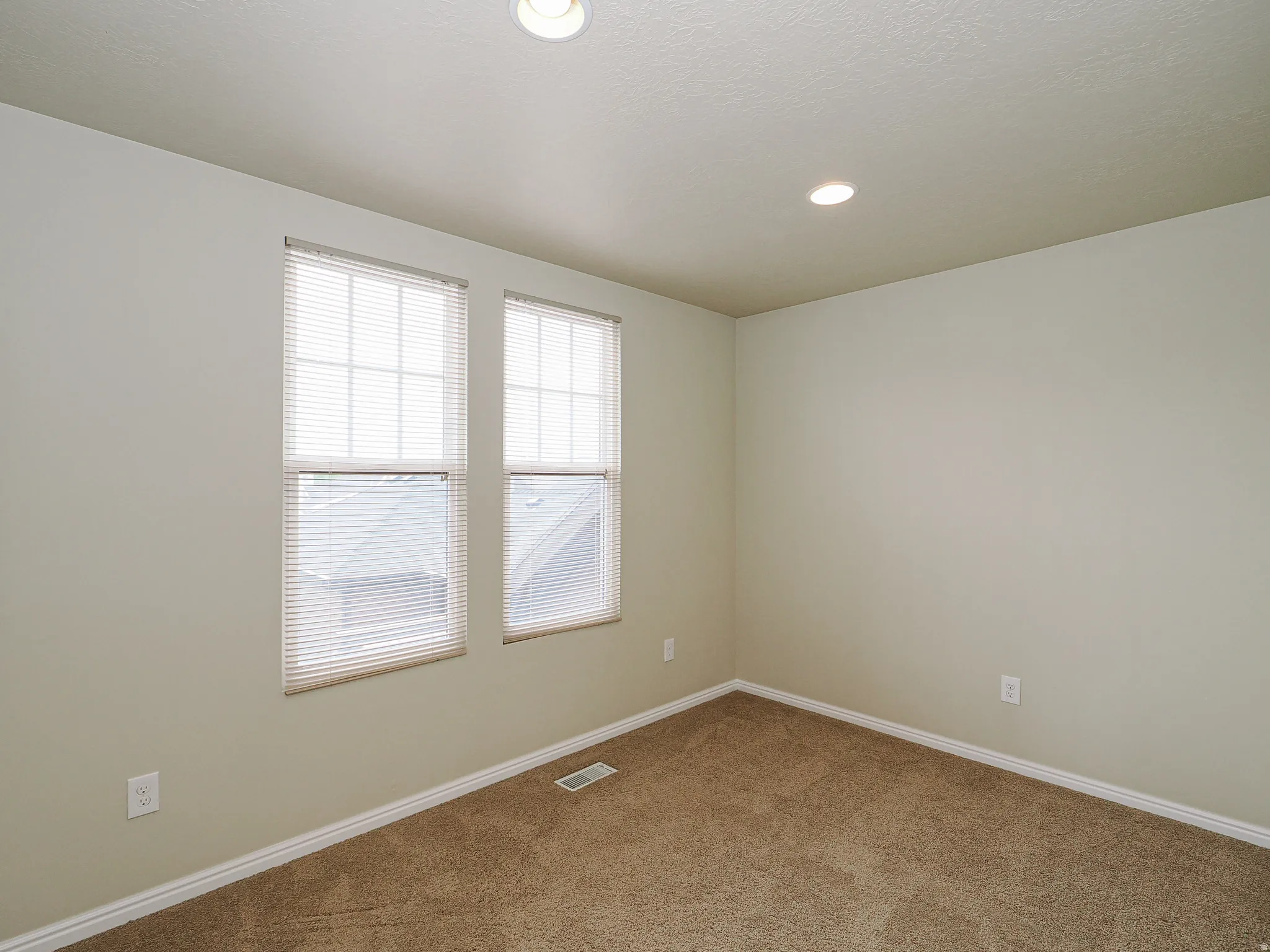 Neutral-toned interior featuring two windows with horizontal blinds, recessed ceiling lighting, and wall-to-wall carpeting