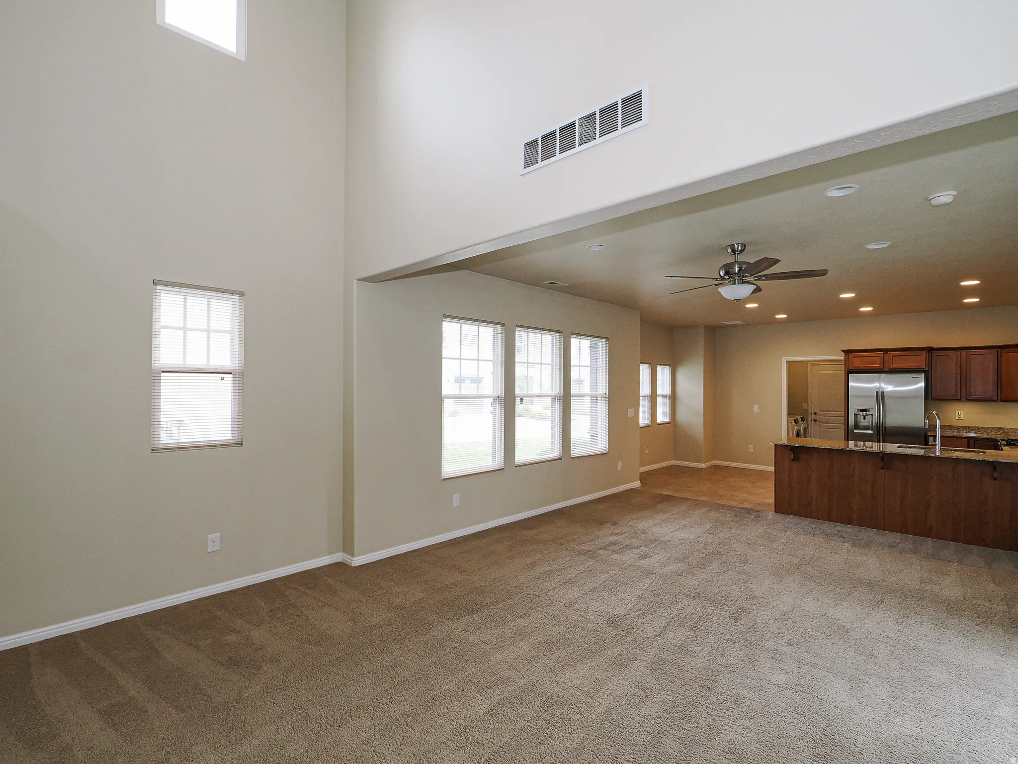Spacious living area featuring high ceilings, ample natural light from multiple windows, and plush carpeting