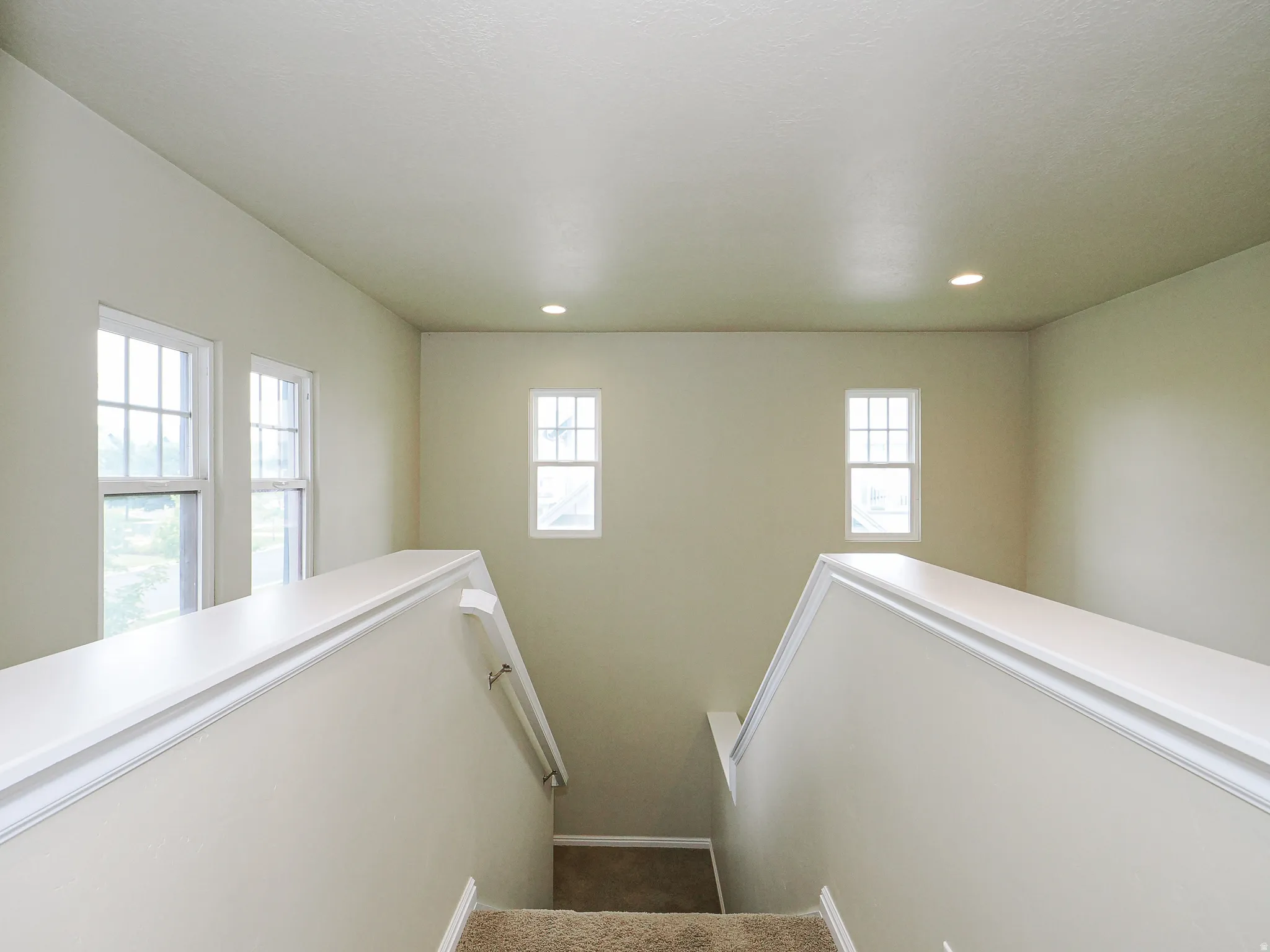 Stairwell with neutral wall paint, white trim, recessed lighting, and multiple windows with grid patterns