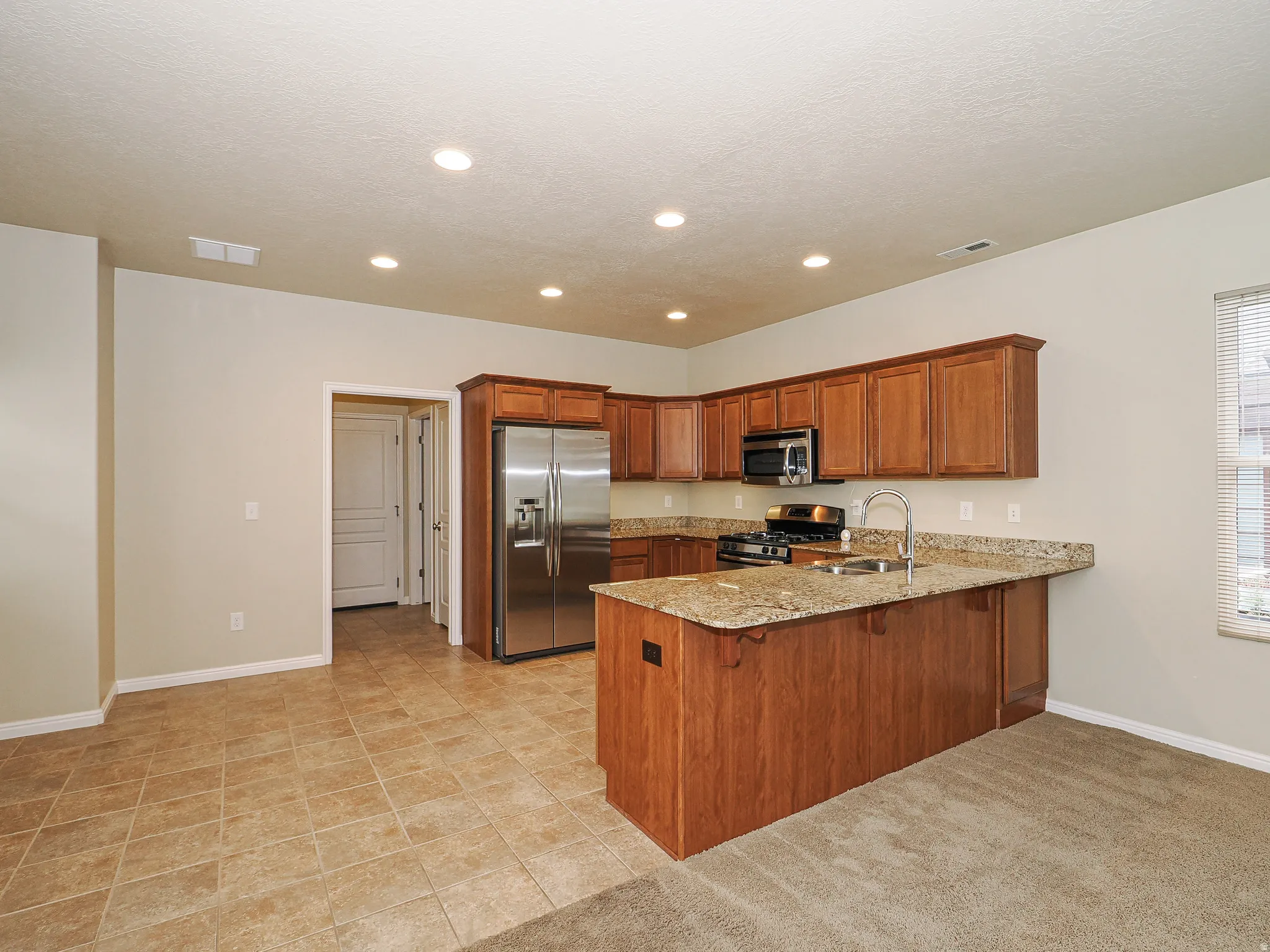 Kitchen featuring wood cabinetry, stainless steel appliances, granite-style countertops, and recessed lighting
