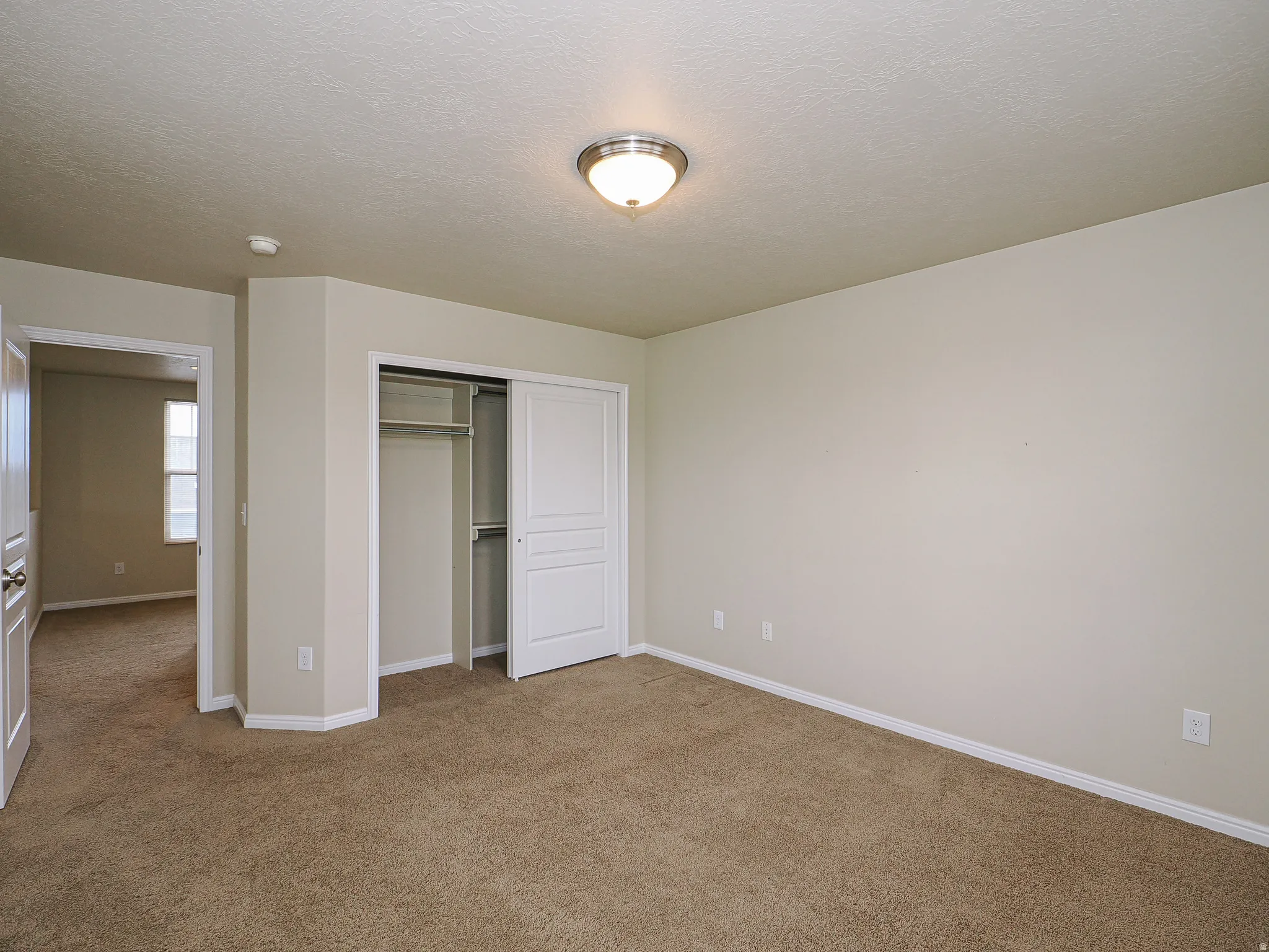 Neutral-toned room featuring plush brown carpeting, light beige walls, and white baseboards