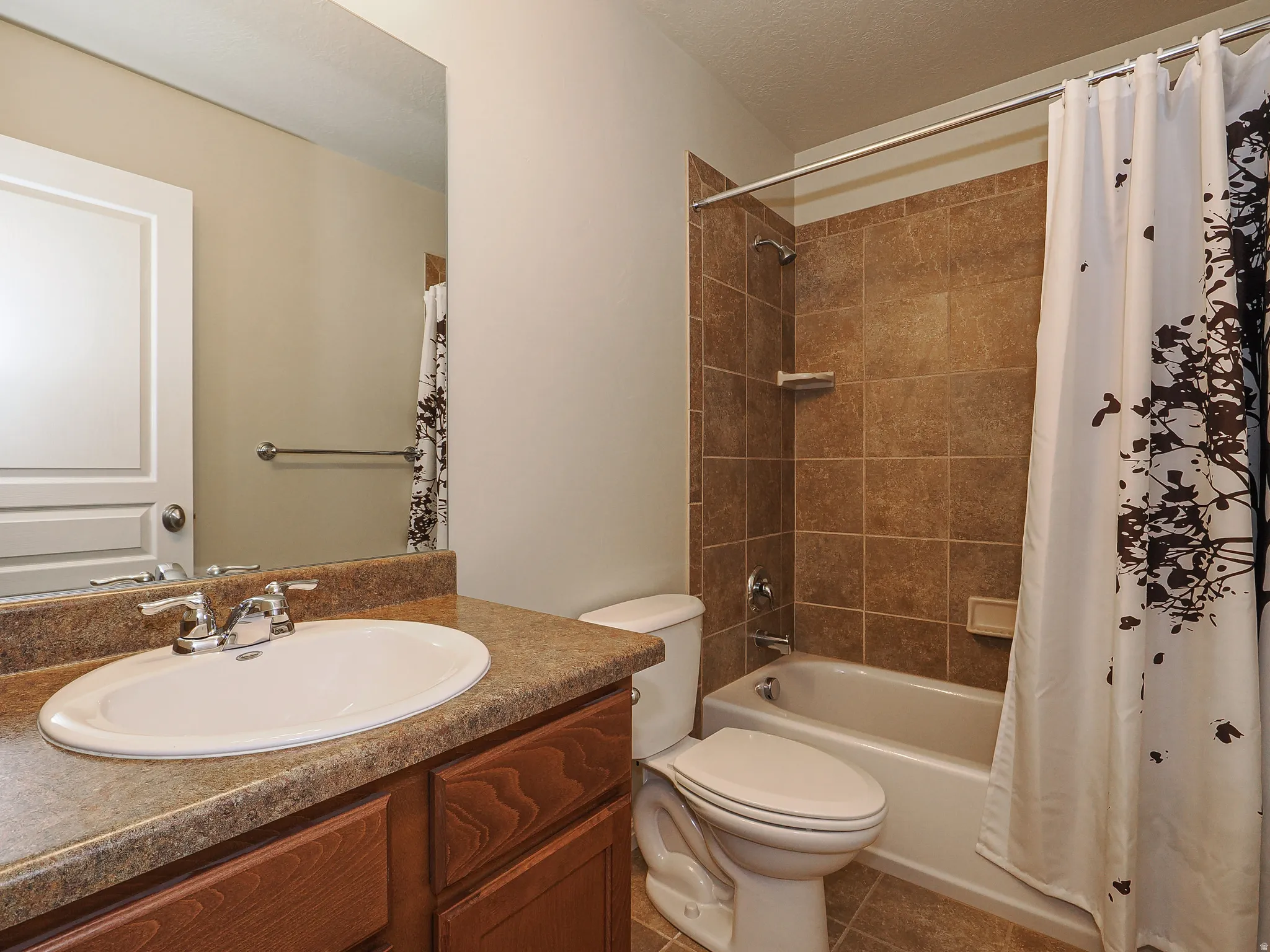 Bathroom featuring a wood-finish vanity with a built-in sink, a speckled countertop, a large mirror, and a tiled shower-tub combination