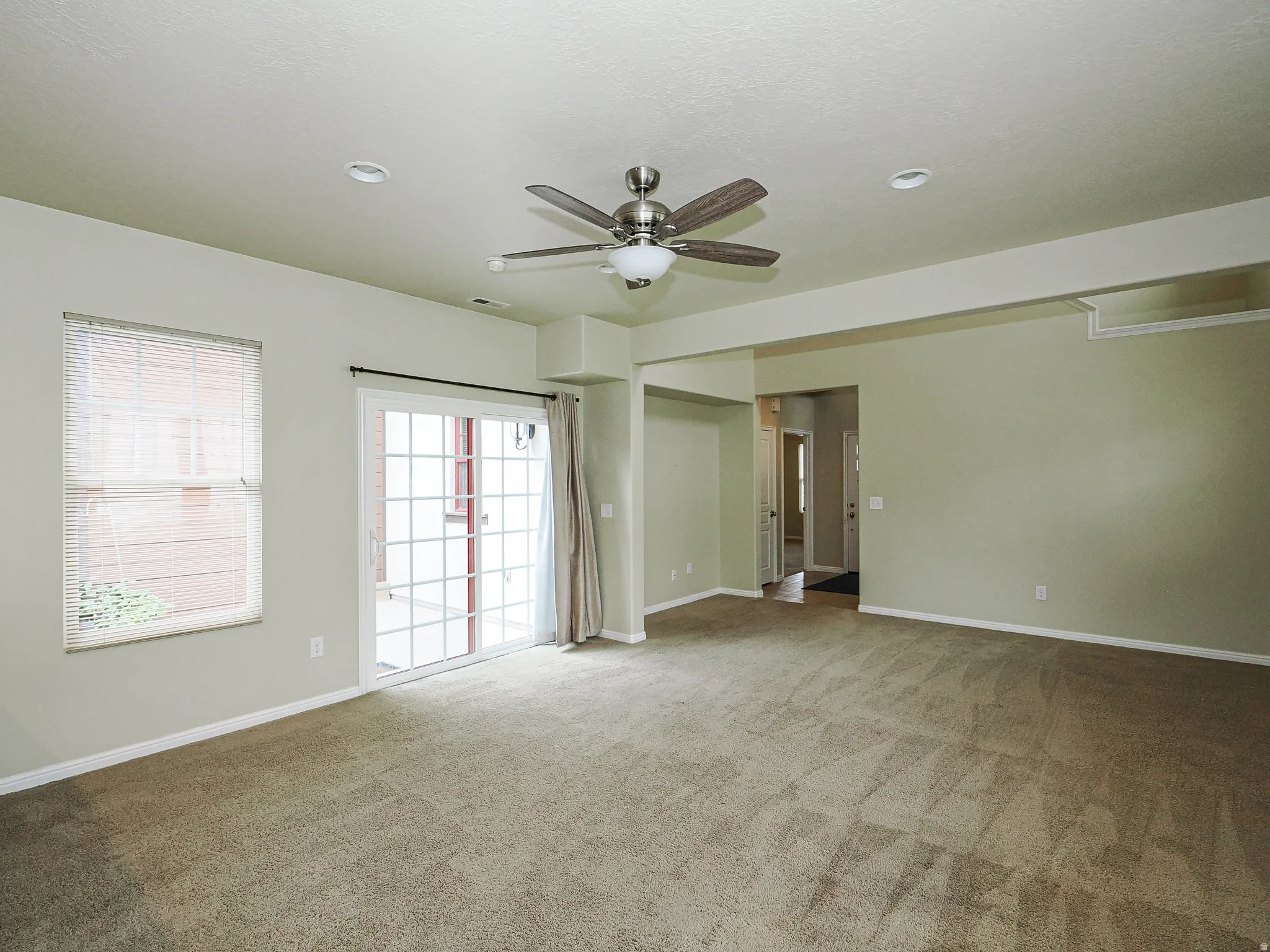 Spacious room featuring neutral carpeting, a ceiling fan with integrated lighting, and recessed overhead lighting