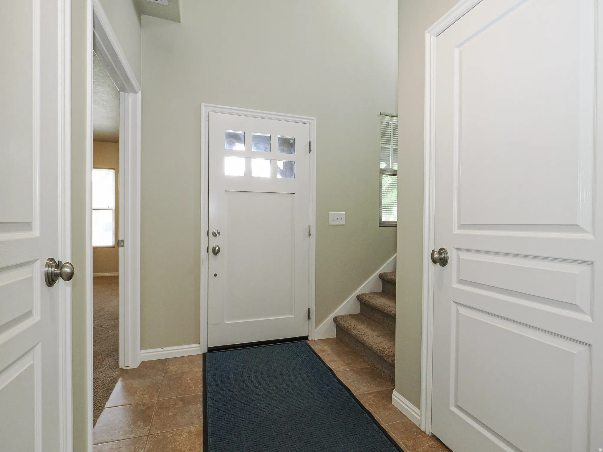 Entryway featuring a white paneled front door with frosted glass panels, tile flooring, carpeted stairs, and light neutral wall paint
