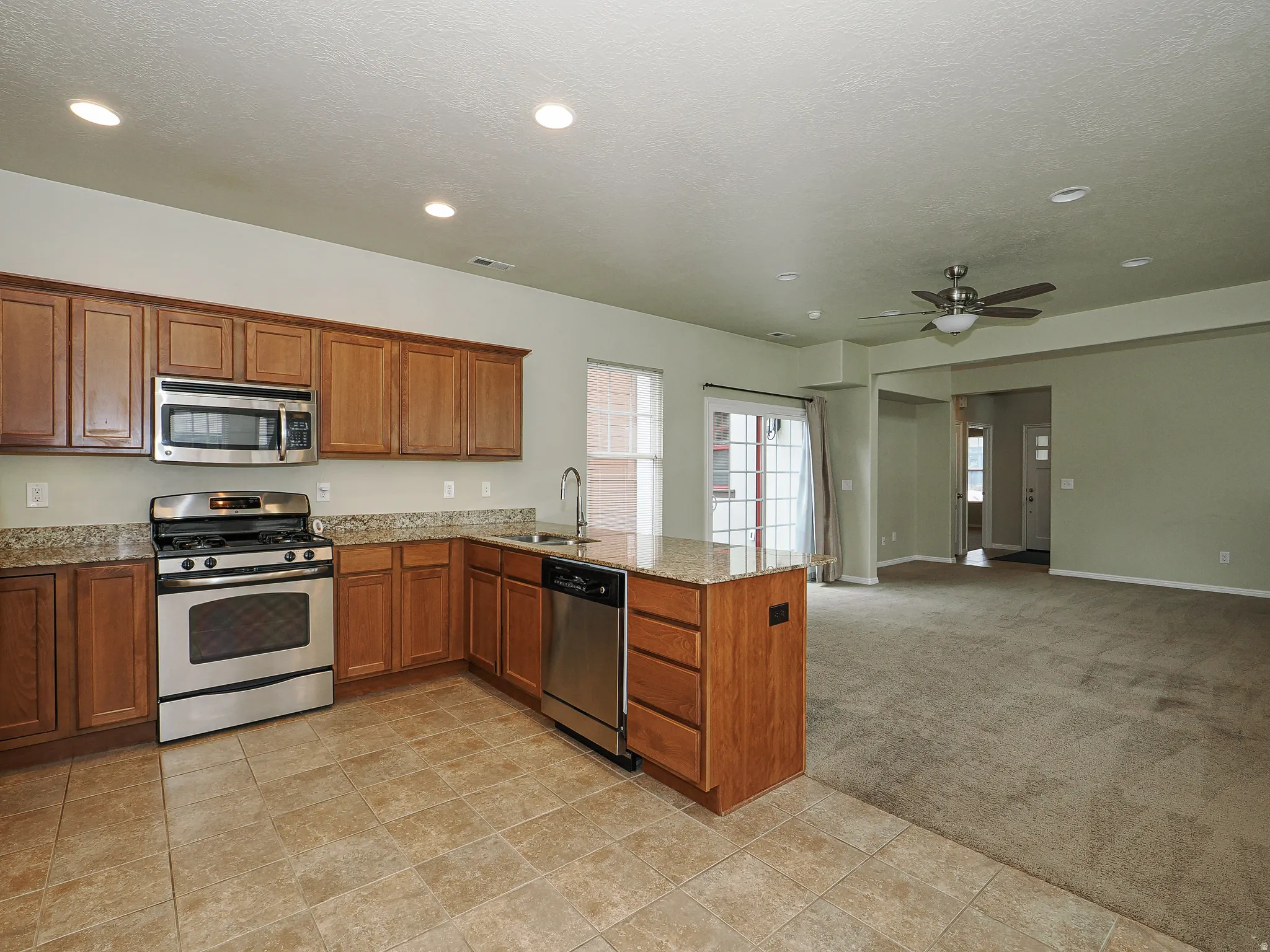 Kitchen featuring granite countertops, wood-finish cabinetry, stainless steel appliances, and tile flooring