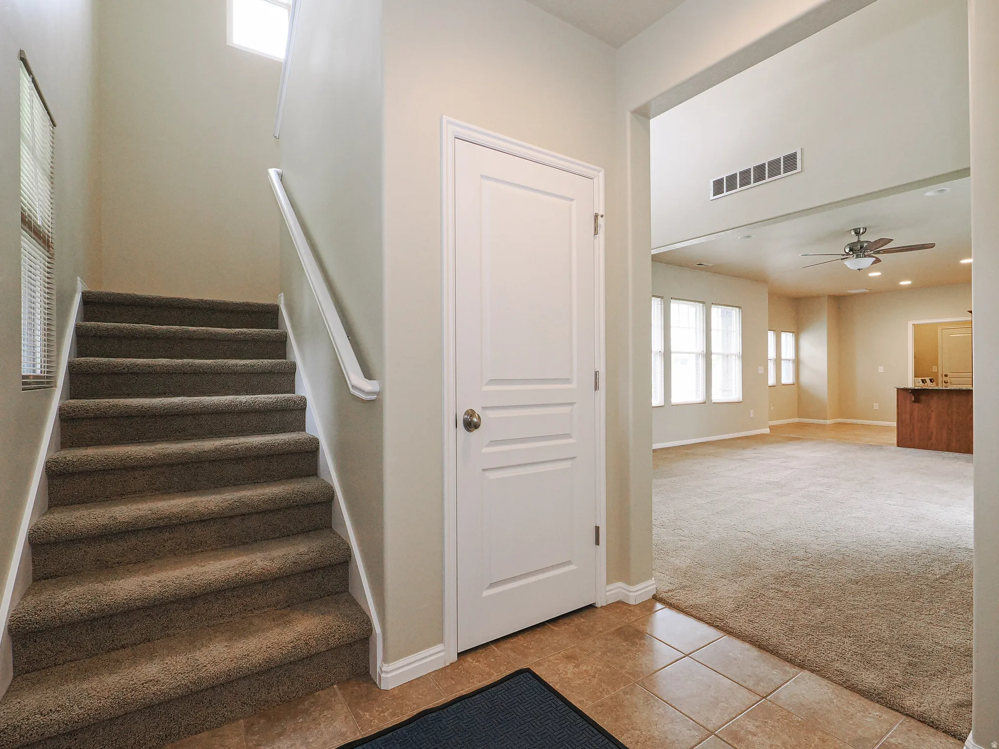 Foyer featuring a carpeted staircase with white handrail, tiled flooring, and an adjacent paneled door