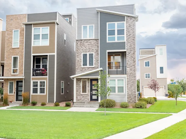 Modern townhome facade featuring gray siding, stone accents, multiple large windows, a covered entry, and a front balcony