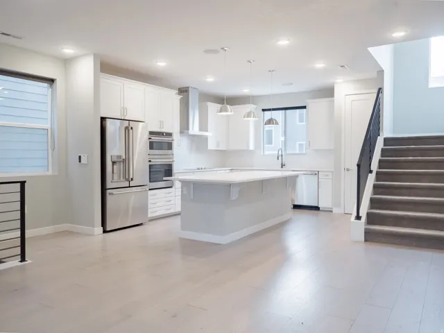 Open-concept kitchen featuring white cabinetry, stainless steel appliances, a central island with pendant lighting, and light wood-finish flooring