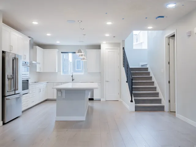Open-concept kitchen and living area featuring light wood-finish flooring, white cabinetry, a central island with a light-colored countertop, and stainless steel appliances