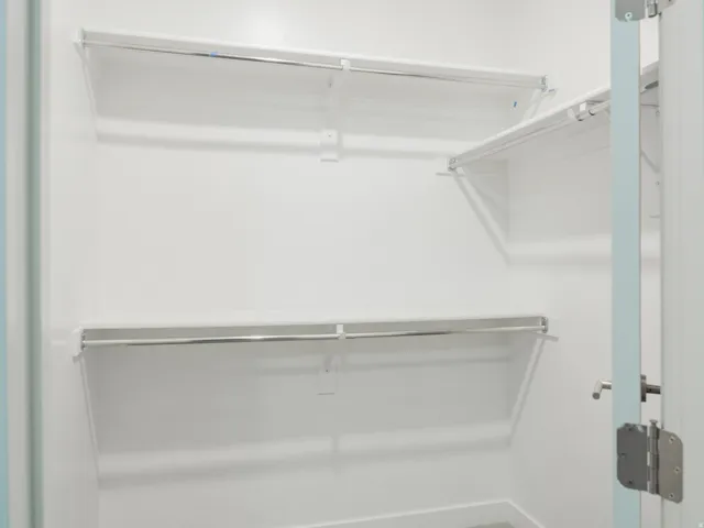 Walk-in closet with white shelving, chrome hanging rods, and white wall finishes