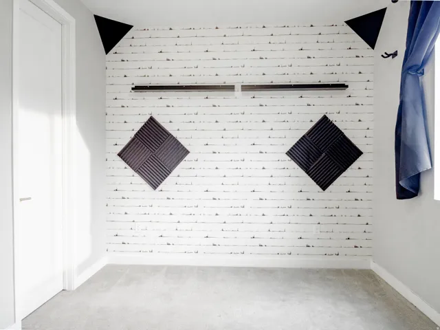 Accent wall with a patterned finish, wall-mounted sound dampening panels, neutral carpeting, and a white interior door with a lever handle
