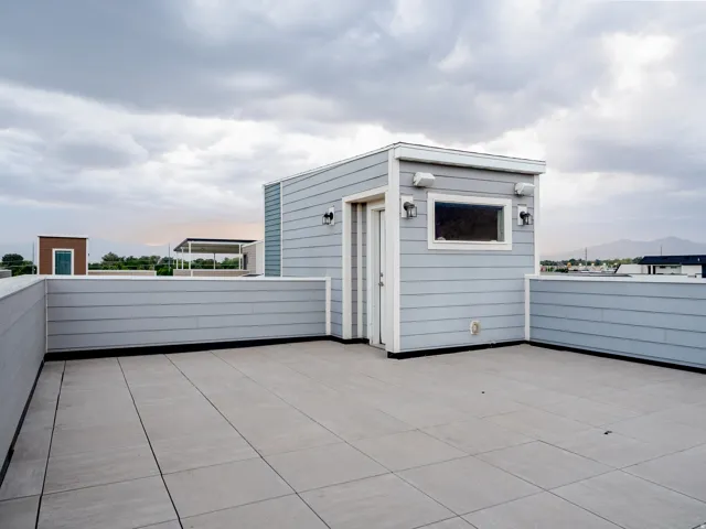 Spacious rooftop deck featuring large format tile flooring and a dedicated access structure with horizontal siding and exterior lighting