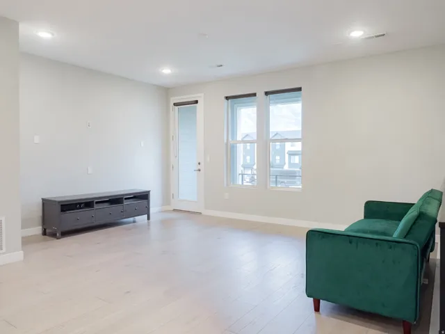 Spacious living area featuring light-toned wood-finish flooring, recessed lighting, multiple windows, and a glass-paneled door
