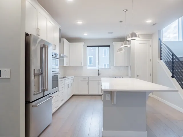 Modern kitchen featuring stainless steel appliances, white cabinetry, a large kitchen island with counter seating, a white subway tile backsplash, and light wood-finish flooring