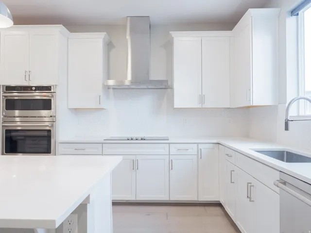 Modern kitchen featuring white shaker cabinetry, stainless steel appliances, a herringbone tile backsplash, and light-tone countertops