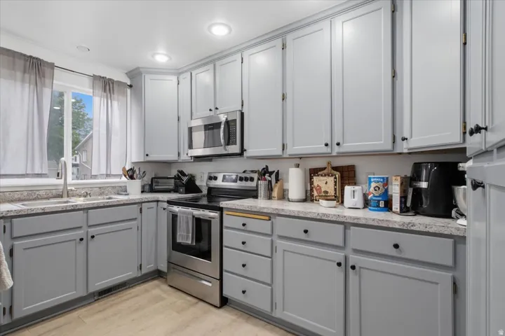 Kitchen featuring light gray cabinetry with black hardware, stainless steel appliances, and light-toned countertops